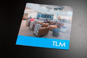 Square brochure for TLM featuring a photo of students sitting in modern brown, white, and black chairs.