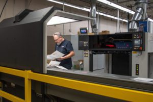 Man in navy tshirt and glasses reviewing paper at printing press